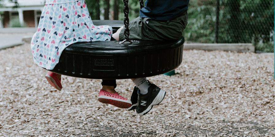 A boy and a girl sitting on a tire swing that is hanging