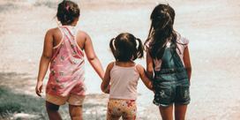 Three kids holding hands while looking out at the tide on a beach