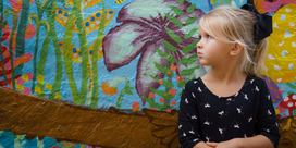 A young girl posing in front of a wall painted with a colorful flower