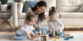 a woman and two children sitting on the floor in front of a sofa in a living room. They are playing with alphabet blocks.