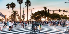lively intersection in LA with palm trees, bike riders and pedestrians