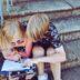 Two children huddled together writing in a notebook