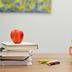 An apple with a pile of colorful books resting upon a wooden desk