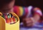 Yellow container full of colorful pencil, with a boy drawing in the background