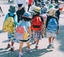 Four children walking in line, wearing backpacks and hats