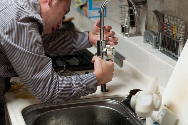 A man from a plumbing service company observing plumbing problems in the kitchen sink.