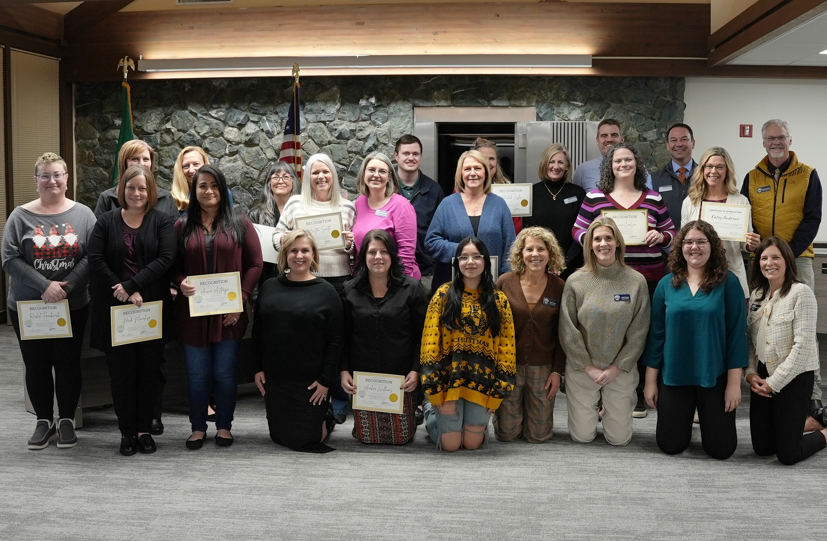 A group of people stand and kneel in a room, holding certificates of recognition.