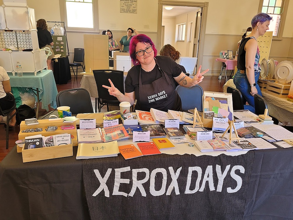 Marijke standing behind the xerox days stall with a table full of assorted zines.