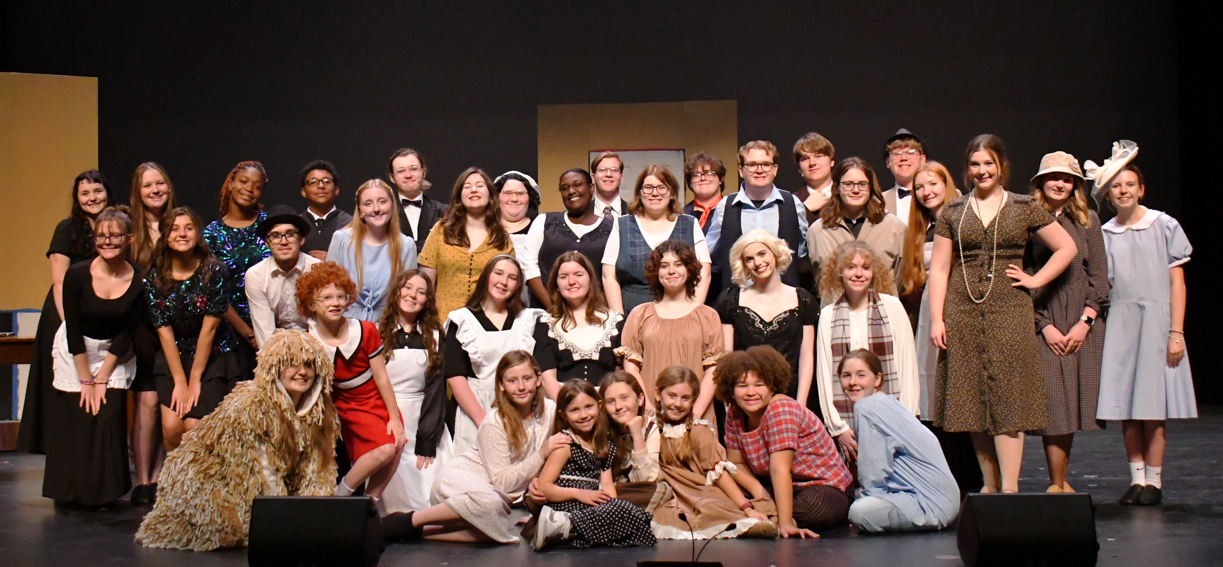 Group photo of about 30 people on stage in costume for "Annie."