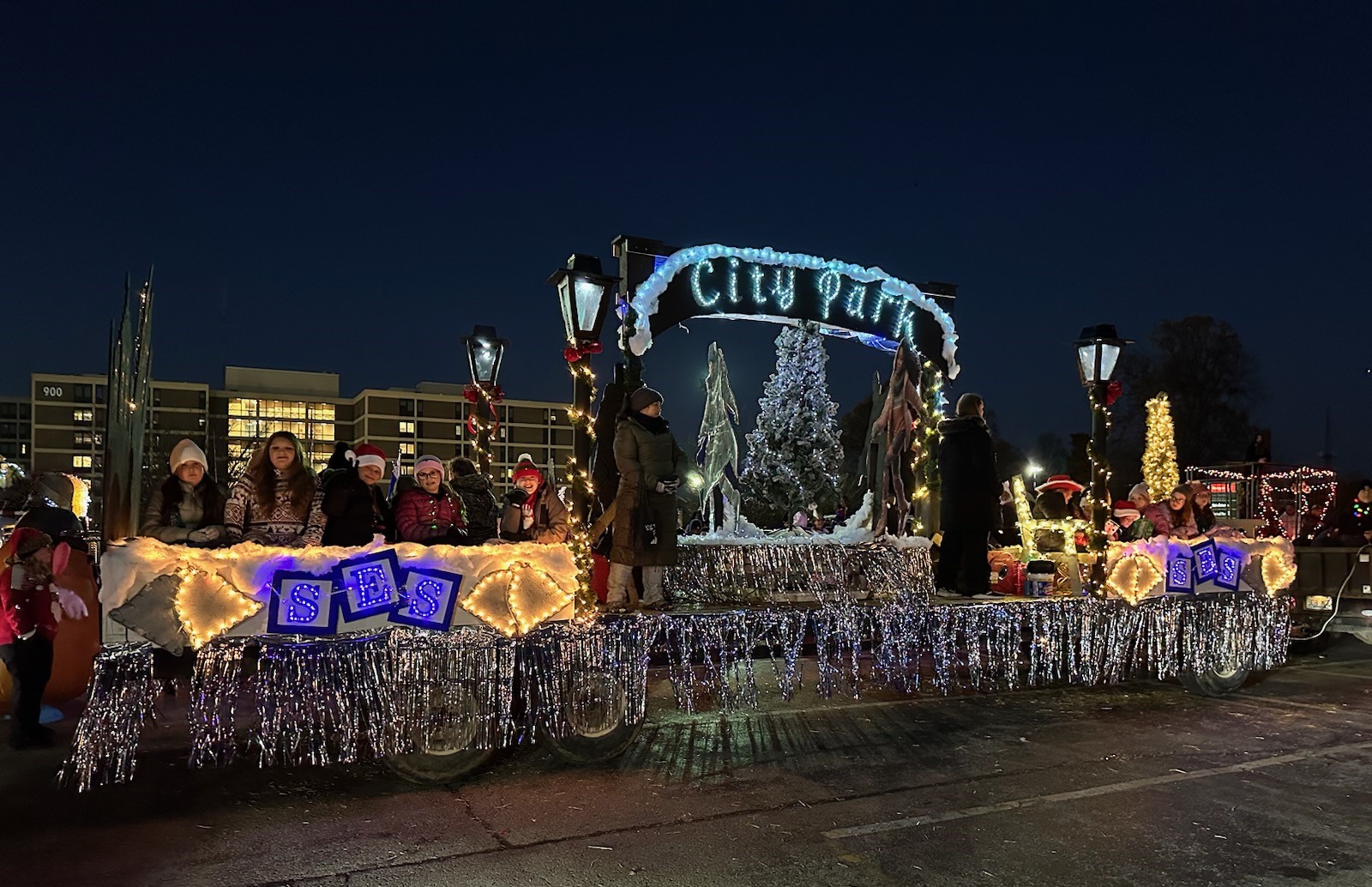 About 11 people ride a float with silver fringe, the letters "SES" and the words "City Park"