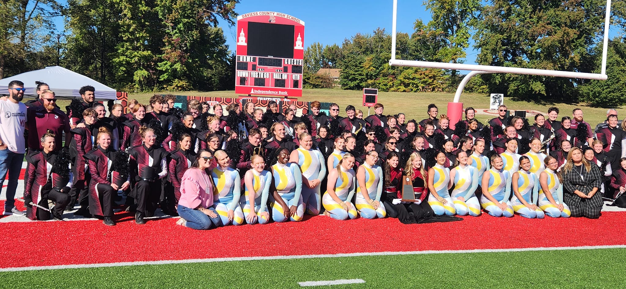 Group photo of band members in maroon and black and others in front row in light blue and yellow.