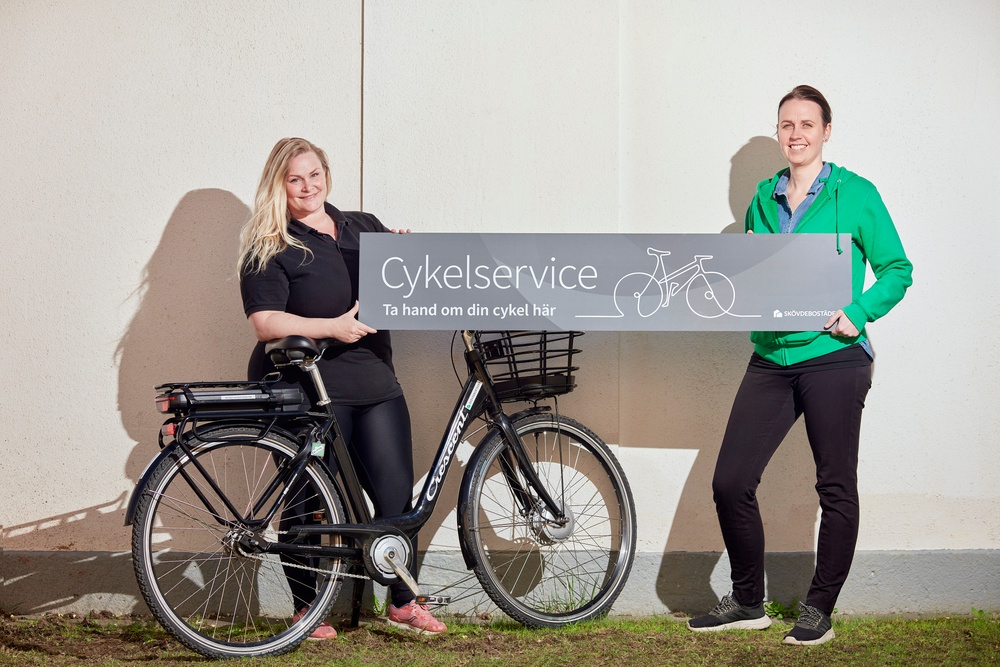 Distriktsassistenterna Caroline Sonestedt och Helen Toftgren står tillsammans med en skylt och en cykel. 
