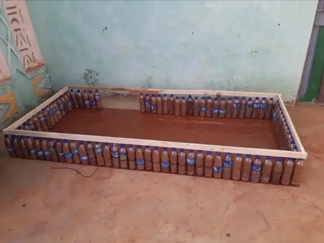 Ecobricks, made out of plastic water bottles, with a wooden frame on top to create a raised garden bed, sitting outside in someone's backyard.