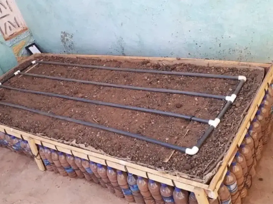 A raised garden bed sitting in someone's backyard, filled with dirt, a plastic irrigation system, and ecobricks.