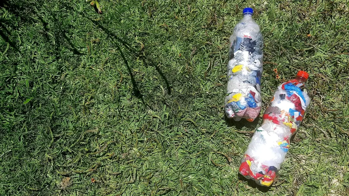 Two ecobricks formed by putting non-biodegradable plastic waste into plastic water bottles, sitting on top of green grass.