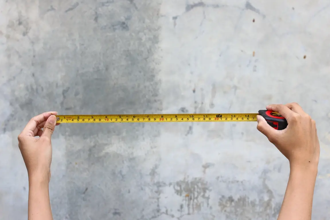 Two hands stretch out a ruler for measuring against a grey outdoor wall.