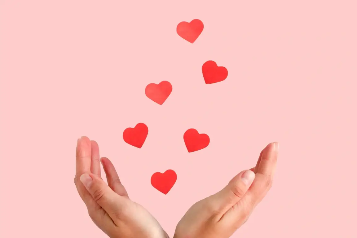 Open hands spreading love in the form of paper hearts floating away from them.