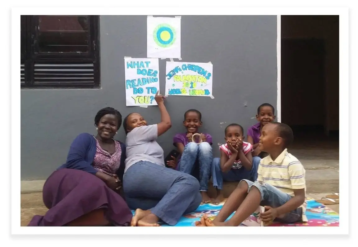 Four women lay smiling under Idealist posters that ask, "What does reading mean to you?"