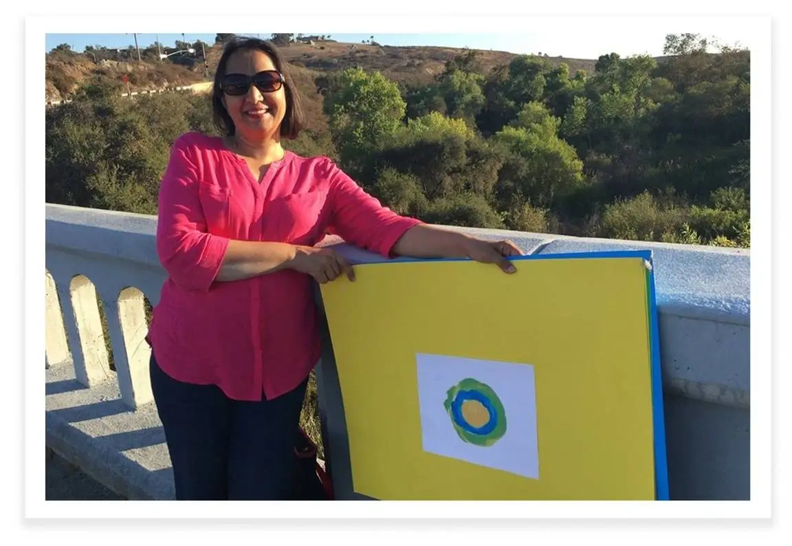 A smiling woman holds up a yellow poster with the Idealist logo on it.