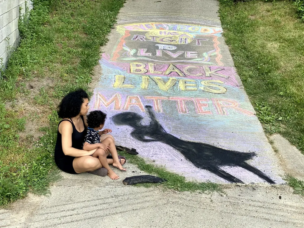 Moraya Seeger DeGeare, of To My Old Racist Earth, and her son sitting by a Black Lives Matter chalk mural