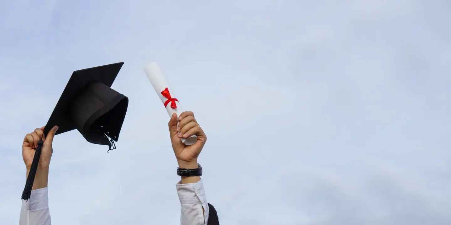 a photograph of a grad student holding a graduation cap and diploma.