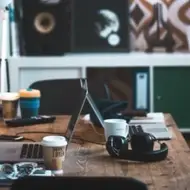 A work desk with two laptops, headphones and cups of coffee.