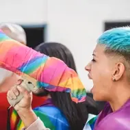 A photograph of a young person with short, blue-dyed hair yelling into a megaphone at an LGBTQ+ pride demonstration.