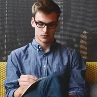 A man with glasses sitting and writing.