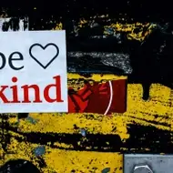 Adesivo escrito "be kind"com a figura de um coração em uma parede artística.