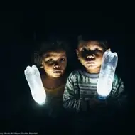 Um menino e uma menina, no escuro, com garrafas plásticas que emanam luz do seu interior