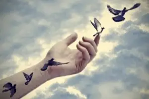 Una mano extendida en la que está dibujada la secuencia del vuelo de una paloma hasta llegar a su dedo donde hay una paloma volando
