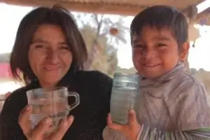 Madre de escasos recursos sosteniendo a su hijo y cada uno con un vaso de agua limpia