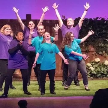 Actors with disabilities raise their arms and belt out the final number of the show.