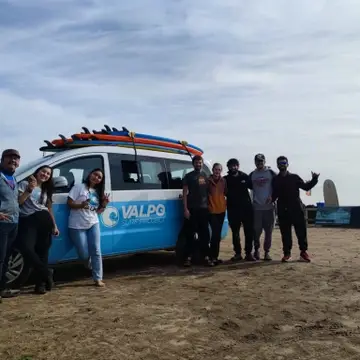Group of people standing in front of Valpo Surf Project van with surfboards on top