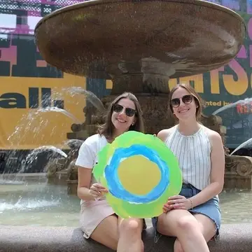 Two people pose by a fountain with the Idealist logo between them.