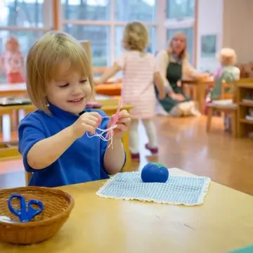 A young child in a Montessori classroom sews independently.