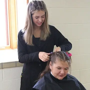 cosmetology student braiding another student's hair