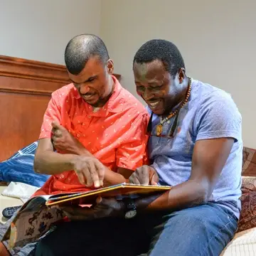 Two gentlemen reading on a bed smiling