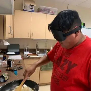 A student wearing a red shirt and learning shades cooks something in the Saavi kitchen.