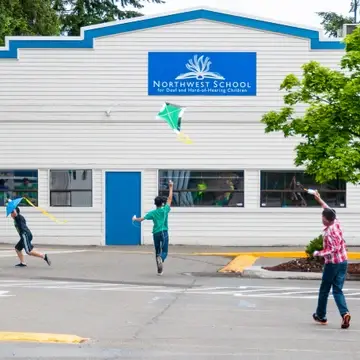 Three middle school boys fly kites in front of the school.