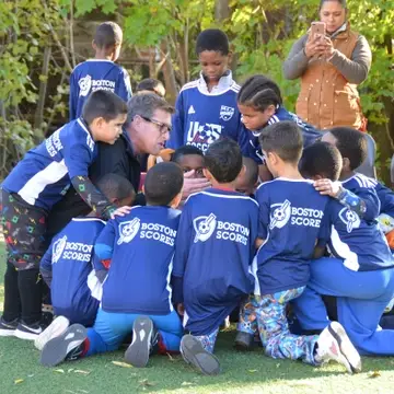 group of elementary school-aged male soccer players gathered around their coach in a huddle