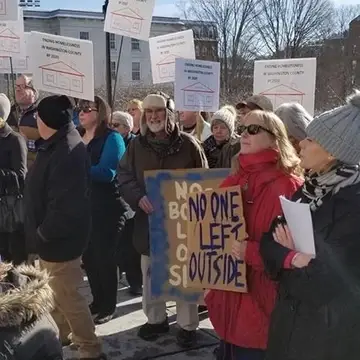 People with signs wearing coats and hats standing outside for a rally at the VT statehouse.