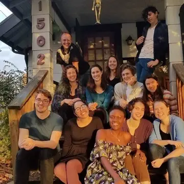 Group of current Portland QVS Fellows sitting on steps to the Portland QVS house with Local Alumni. A group of about 15 diverse young adults.