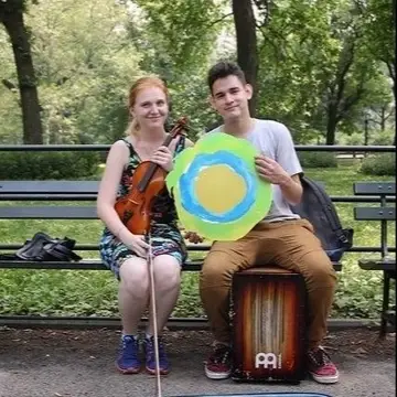 Two people on a park bench pose with the Idealist logo between them.