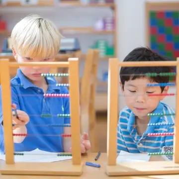 Montessori students work on math using a large bead frame