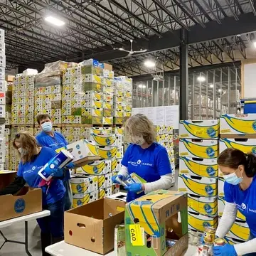 Volunteers at Good Shepherd Food Bank of Maine in front of a wall of banana boxes in the Auburn Distribution Center.