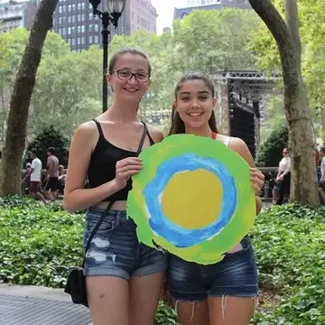 Two women in Union Square park pose with the Idealist logo between them.
