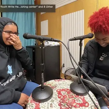 Two brown teens in black hoodies laughing at microphones