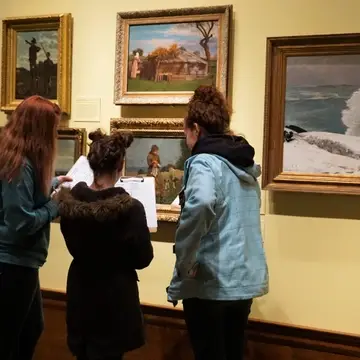 Three teenage students working on clipboards in front of artwork
