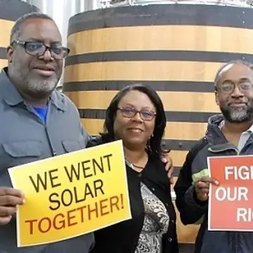 Group of three individuals holding up signs that say we went solar together and fight for our energy rights